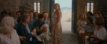Movie still from “Mamma Mia! Here We Go Again” (2018), directed by Ol Parker – A group of people gathered around a woman holding a baby; Wide shot, Over the shoulder angle