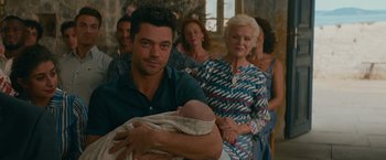 Movie still from “Mamma Mia! Here We Go Again” (2018), directed by Ol Parker – A man holding a baby in front of a group of people; Close Up shot, Over the shoulder angle