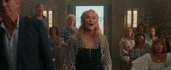 Movie still from “Mamma Mia! Here We Go Again” (2018), directed by Ol Parker – A woman sings in front of a group of other women; Medium shot, Over the shoulder angle