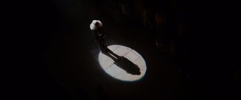 Movie still from “Mamma Mia! Here We Go Again” (2018), directed by Ol Parker – A person standing in the dark with a light shining on them; Extreme Wide shot, Overhead angle