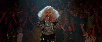 Movie still from “Mamma Mia! Here We Go Again” (2018), directed by Ol Parker – A woman in a white wig singing into a microphone in front of a crowd; Medium shot, High angle