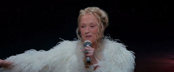 Movie still from “Mamma Mia! Here We Go Again” (2018), directed by Ol Parker – A woman in a white fur coat is holding a microphone; Close Up shot, Overhead angle