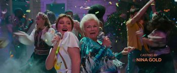 Movie still from “Mamma Mia! Here We Go Again” (2018), directed by Ol Parker – Two older women singing into microphones at a party; Medium shot, Low angle