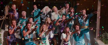 Movie still from “Mamma Mia! Here We Go Again” (2018), directed by Ol Parker – A group of people singing in front of confetti; Wide shot, High angle