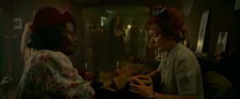 Movie still from “Mrs. Harris Goes to Paris” (2022), directed by Anthony Fabian – Two women sitting at a table with a glass of wine in front of them; Medium shot, High angle