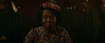 Movie still from “Mrs. Harris Goes to Paris” (2022), directed by Anthony Fabian – An older black woman wearing a floral shirt and a flower crown; Close Up shot, Over the shoulder angle