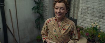 Movie still from “Mrs. Harris Goes to Paris” (2022), directed by Anthony Fabian – An older woman sitting in front of a plant; Medium shot, High angle