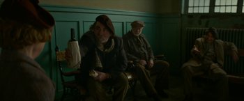 Movie still from “Mrs. Harris Goes to Paris” (2022), directed by Anthony Fabian – Two older men sitting on a bench in a room; Medium shot, Low angle