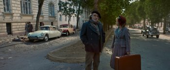 Movie still from “Mrs. Harris Goes to Paris” (2022), directed by Anthony Fabian – An older man and woman standing on the side of the road; Wide shot, High angle
