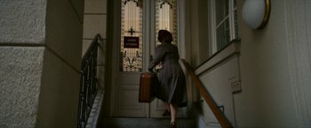Movie still from “Mrs. Harris Goes to Paris” (2022), directed by Anthony Fabian – A woman in a gray dress carrying a suitcase down a flight of stairs; Wide shot, Low angle