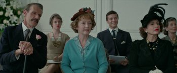 Movie still from “Mrs. Harris Goes to Paris” (2022), directed by Anthony Fabian – Three people sitting in a room , one of whom is wearing a hat; Medium shot, Over the shoulder angle