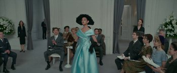 Movie still from “Mrs. Harris Goes to Paris” (2022), directed by Anthony Fabian – A woman in a blue dress is standing in front of a group of people; Wide shot, Low angle
