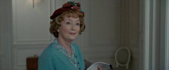 Movie still from “Mrs. Harris Goes to Paris” (2022), directed by Anthony Fabian – An older woman wearing a hat and holding a book; Close Up shot, Over the shoulder angle