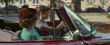 Movie still from “Mrs. Harris Goes to Paris” (2022), directed by Anthony Fabian – A woman sitting in the driver's seat of a red car; Medium shot, Over the shoulder angle