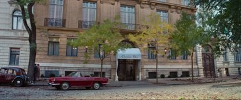 Movie still from “Mrs. Harris Goes to Paris” (2022), directed by Anthony Fabian – A red car parked in front of a building; Wide shot, High angle