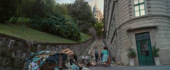 Movie still from “Mrs. Harris Goes to Paris” (2022), directed by Anthony Fabian – Two women walking down a street with a pile of trash; Extreme Wide shot, High angle