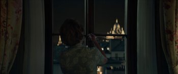 Movie still from “Mrs. Harris Goes to Paris” (2022), directed by Anthony Fabian – A woman standing in front of a window at night; Medium shot, Over the shoulder angle