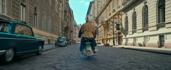 Movie still from “Mrs. Harris Goes to Paris” (2022), directed by Anthony Fabian – A person on a motor scooter riding down a street; Wide shot, High angle