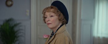 Movie still from “Mrs. Harris Goes to Paris” (2022), directed by Anthony Fabian – An older woman wearing a hat and holding a flower; Close Up shot, Over the shoulder angle