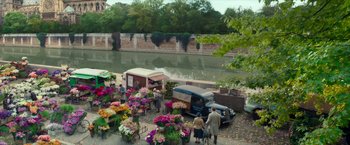 Movie still from “Mrs. Harris Goes to Paris” (2022), directed by Anthony Fabian – A group of people standing next to a flower market; Extreme Wide shot, High angle