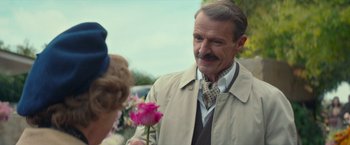 Movie still from “Mrs. Harris Goes to Paris” (2022), directed by Anthony Fabian – An older man holding a pink rose next to an older woman; Close Up shot, Over the shoulder angle