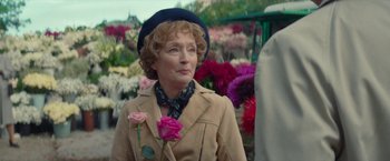Movie still from “Mrs. Harris Goes to Paris” (2022), directed by Anthony Fabian – An older woman wearing a hat holding a pink rose; Medium shot, Over the shoulder angle