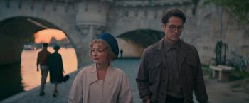 Movie still from “Mrs. Harris Goes to Paris” (2022), directed by Anthony Fabian – A man and a woman standing next to each other in front of a bridge; Medium shot, Over the shoulder angle