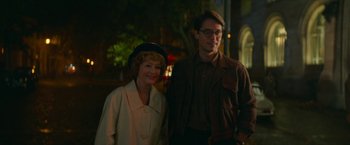Movie still from “Mrs. Harris Goes to Paris” (2022), directed by Anthony Fabian – A man standing next to an older woman in front of a building; Medium shot, Over the shoulder angle