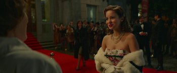 Movie still from “Mrs. Harris Goes to Paris” (2022), directed by Anthony Fabian – A beautiful young woman in a white dress and a fur coat; Medium shot, Over the shoulder angle