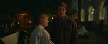 Movie still from “Mrs. Harris Goes to Paris” (2022), directed by Anthony Fabian – A man standing next to an older woman in front of a building; Medium shot, Over the shoulder angle