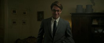Movie still from “Mrs. Harris Goes to Paris” (2022), directed by Anthony Fabian – A man in a suit and tie smiling for the camera; Close Up shot, Over the shoulder angle