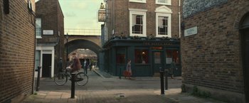 Movie still from “Mrs. Harris Goes to Paris” (2022), directed by Anthony Fabian – People are walking and riding bikes on the sidewalk; Extreme Wide shot, High angle