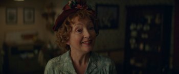 Movie still from “Mrs. Harris Goes to Paris” (2022), directed by Anthony Fabian – An older woman wearing a hat and smiling for the camera; Close Up shot, Over the shoulder angle