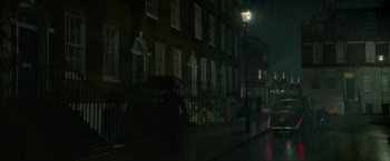 Movie still from “Mrs. Harris Goes to Paris” (2022), directed by Anthony Fabian – A person with an umbrella walking down the street at night; Extreme Wide shot, High angle