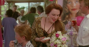 Movie still from “Muriel's Wedding” (1994), directed by P.J. Hogan – A woman in leopard print is holding a cake; Medium shot, Over the shoulder angle