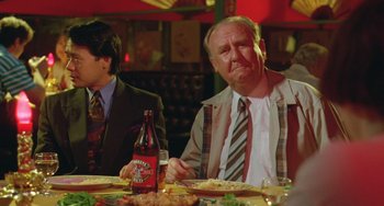 Movie still from “Muriel's Wedding” (1994), directed by P.J. Hogan – A man sitting at a dinner table with a bottle of soda; Medium shot, Over the shoulder angle