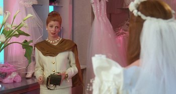 Movie still from “Muriel's Wedding” (1994), directed by P.J. Hogan – A woman in a white dress holding a black purse; Medium shot, Over the shoulder angle