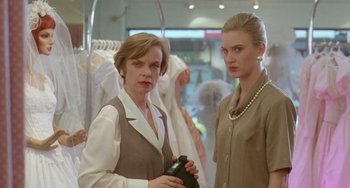 Movie still from “Muriel's Wedding” (1994), directed by P.J. Hogan – Two women are standing next to each other in front of a row of dresses; Medium shot, Low angle