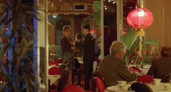 Movie still from “Muriel's Wedding” (1994), directed by P.J. Hogan – A man and a woman standing in a restaurant; Wide shot, Over the shoulder angle