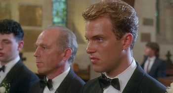 Movie still from “Muriel's Wedding” (1994), directed by P.J. Hogan – Two men in tuxedos are standing next to each other in front of a stained glass window; Close Up shot, Low angle