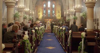 Movie still from “Muriel's Wedding” (1994), directed by P.J. Hogan – A wedding ceremony in a church with a priest standing in front of the pews; Extreme Wide shot, High angle