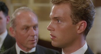 Movie still from “Muriel's Wedding” (1994), directed by P.J. Hogan – A man in a suit and tie next to another man in a tuxedo; Close Up shot, Over the shoulder angle