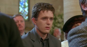 Movie still from “Muriel's Wedding” (1994), directed by P.J. Hogan – A man in a suit and tie in front of a crowd; Close Up shot, Over the shoulder angle