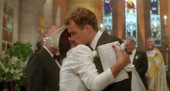 Movie still from “Muriel's Wedding” (1994), directed by P.J. Hogan – A man and a woman kissing in front of other people; Close Up shot, Over the shoulder angle