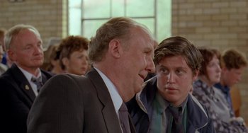 Movie still from “Muriel's Wedding” (1994), directed by P.J. Hogan – A man in a suit talking to another man in a suit; Close Up shot, Over the shoulder angle