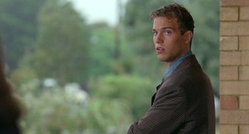 Movie still from “Muriel's Wedding” (1994), directed by P.J. Hogan – A man in a suit looking at the camera with trees in the background; Close Up shot, Over the shoulder angle