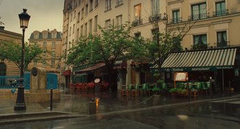 Movie still from “Midnight in Paris” (2011), directed by Woody Allen – A street scene of a rainy day with tables and chairs; Extreme Wide shot, High angle