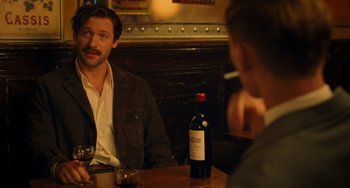 Movie still from “Midnight in Paris” (2011), directed by Woody Allen – A man sitting at a table in front of a bottle of wine; Medium shot, Over the shoulder angle