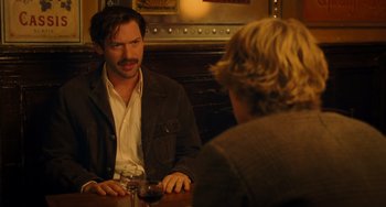 Movie still from “Midnight in Paris” (2011), directed by Woody Allen – A man sitting at a table talking to another man; Medium shot, Over the shoulder angle