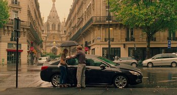 Movie still from “Midnight in Paris” (2011), directed by Woody Allen – A man and a woman standing in front of a black car; Wide shot, High angle